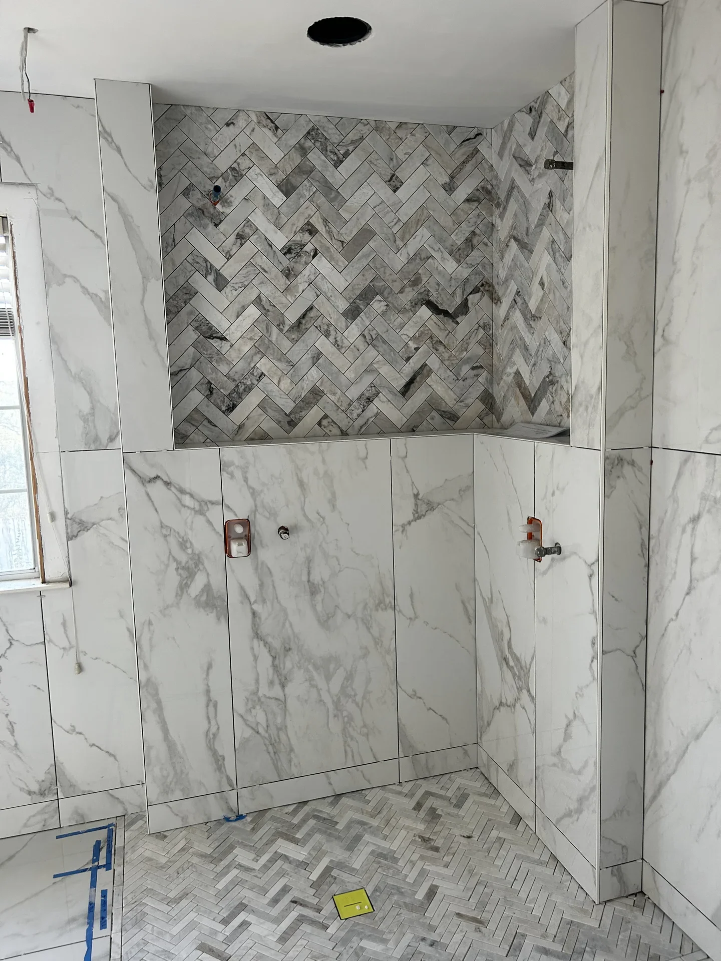 Marble tile shower with herringbone niche and floor by Bowman Built in Redding CA