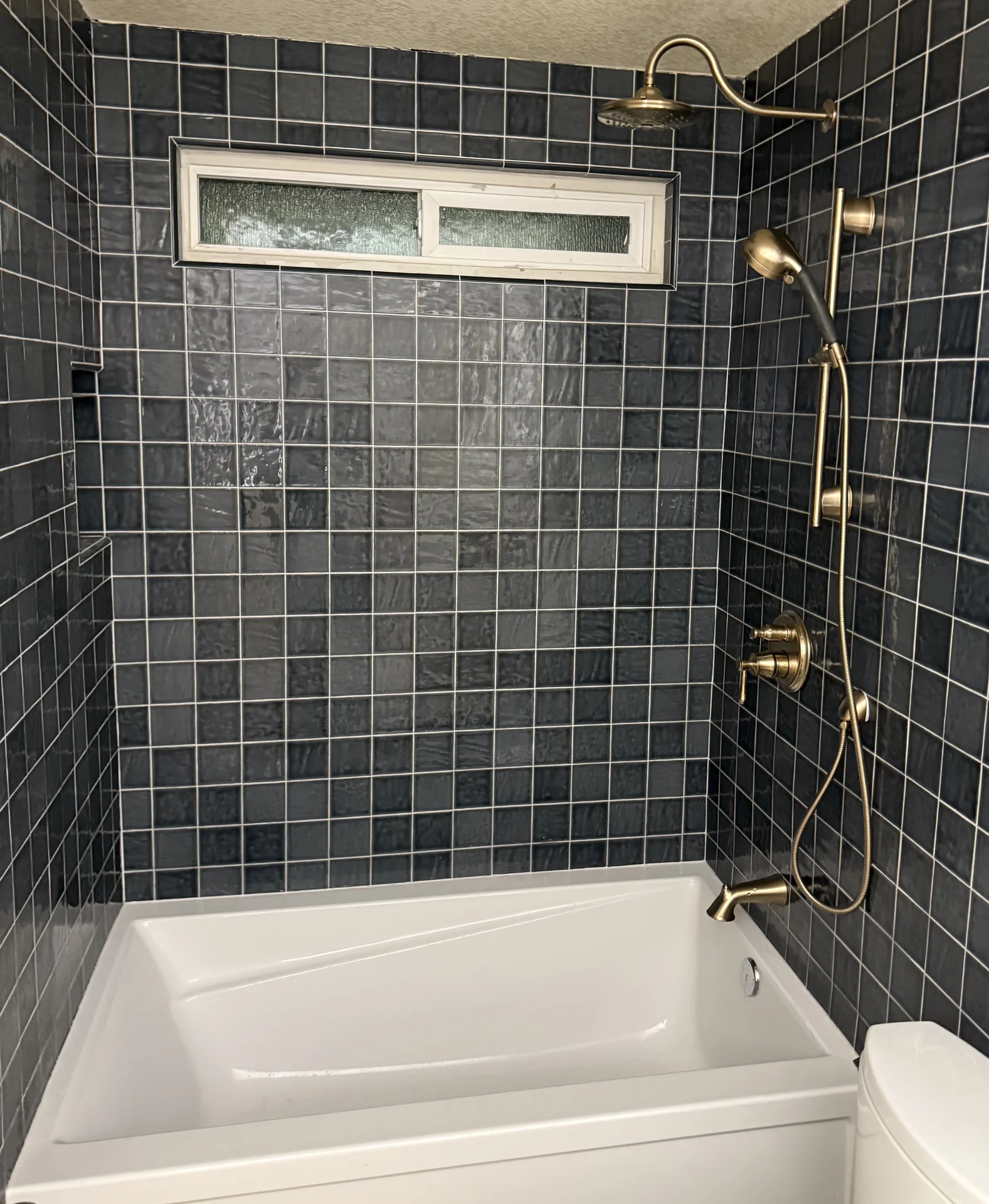 Blue tile bathroom with brass fixtures and white tub
